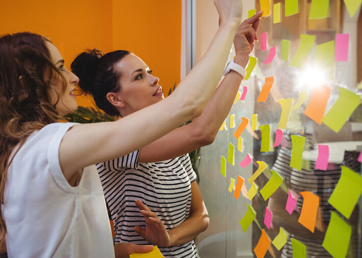 Two young ladies discussing how to sort post-it notes